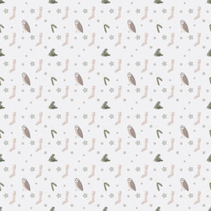 White wrapping paper with an owl, beige socks, pine tree branches and green snowflakes