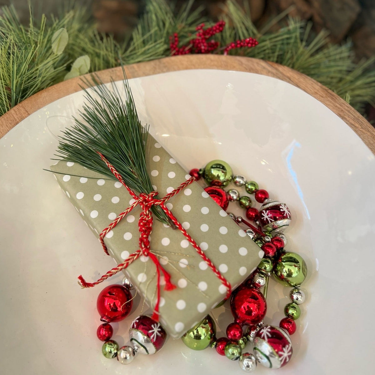 Christmas gift wrapped with green wrapping paper with Christmas ornaments besides it