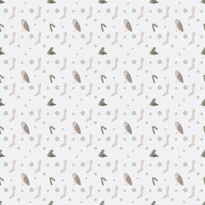 White wrapping paper with an owl, beige socks, pine tree branches and green snowflakes